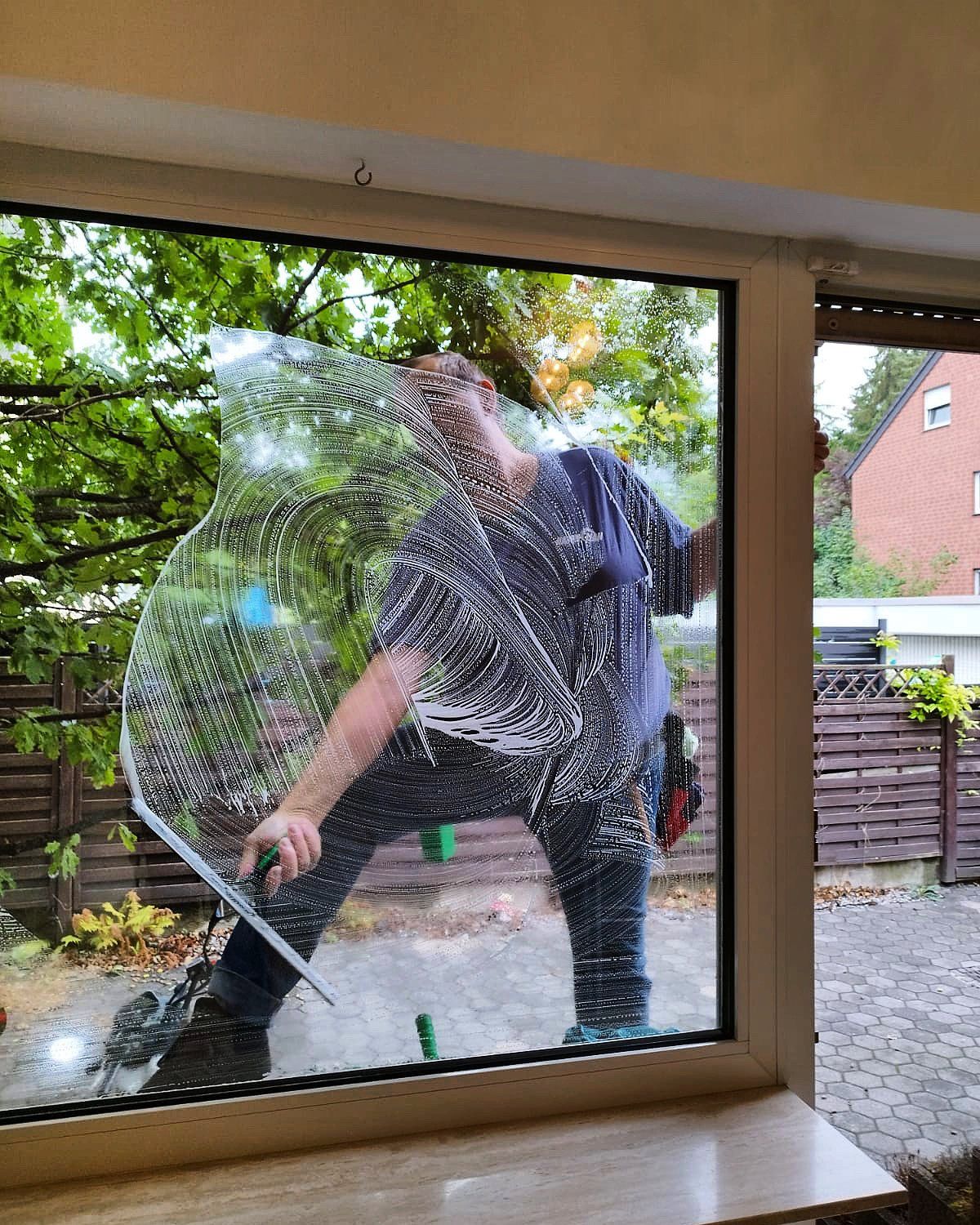 Mitarbeiter von HammClean reinigt eine große Fensterscheibe, auf dem Glas noch der Seifenschaum