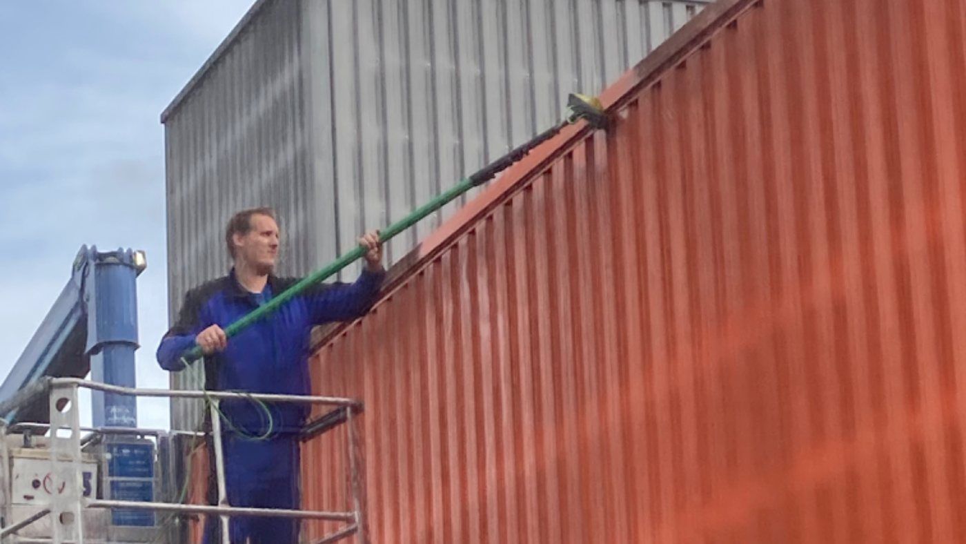 Mitarbeiter von HammClean reinigt von einer Arbeitsbühne aus eine rote Metallfassade